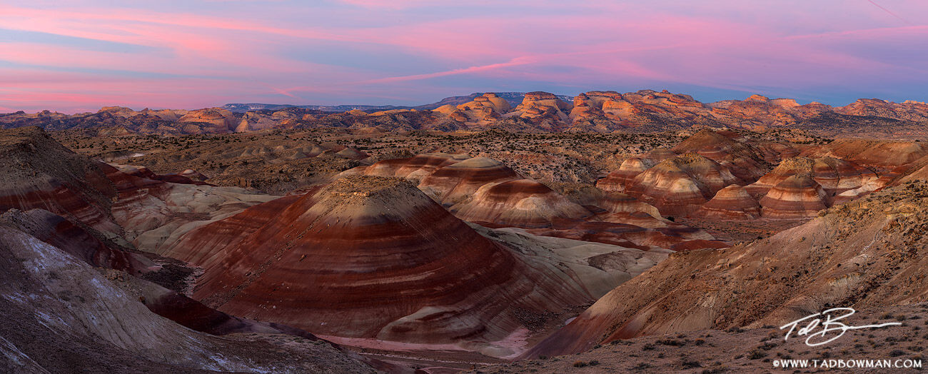 This Utah panorama photo depicts sunrise over bentonite hills and beige sandstone rock formations in the Capitol Reef National...