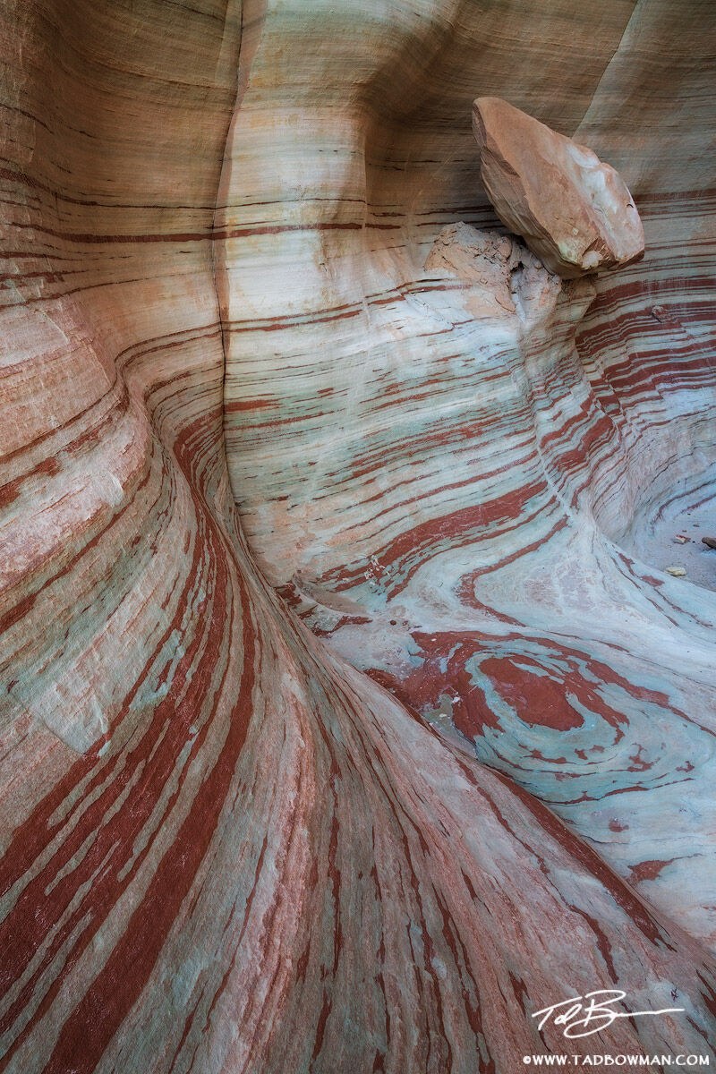 This Utah Desert photo depicts a rock hanging on a ledge in a cove with red striped walls