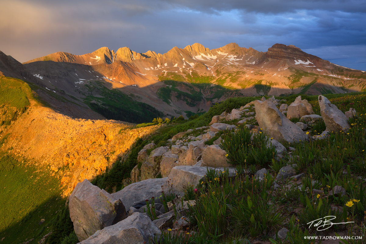 This Colorado mountain photo depicts sunrise on the La Plata mountains with jagged rocks and wildflowers in the foreground.