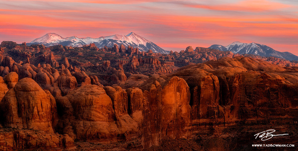 This Utah desert photo depicts a colorful sunset over the La Sal Mountains with rock sandstones in the foreground