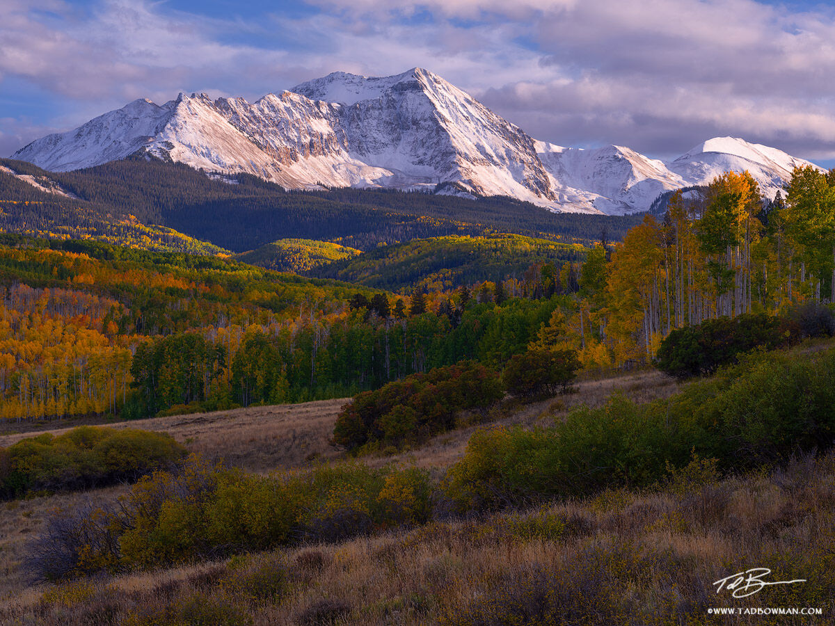 This Colorado mountain photo depicts late afternoon late over a snowy mountain with colorful fall foliage in the foregrund