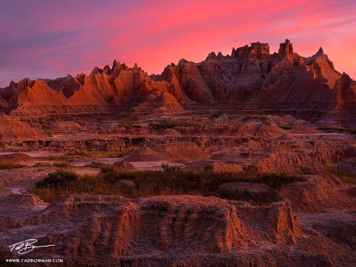 The Kingdom of Dust Warm sunrise light ignites the rugged, layered formations of Badlands National Park, South Dakota, casting deep shadows across...