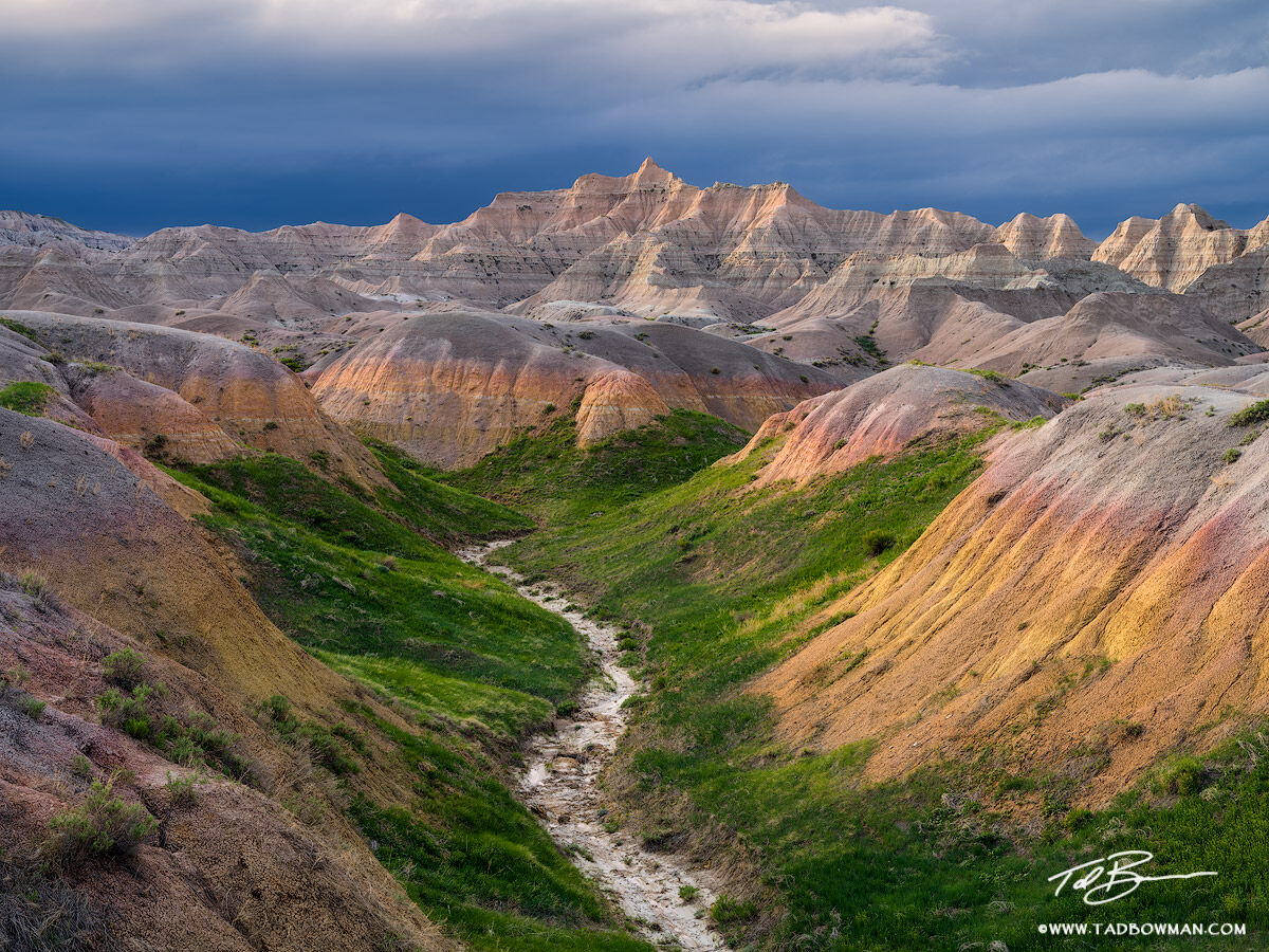 This national park photo depicts late afternoon light glancing off rock formations with a thunderstorm approaching in the Badlands...